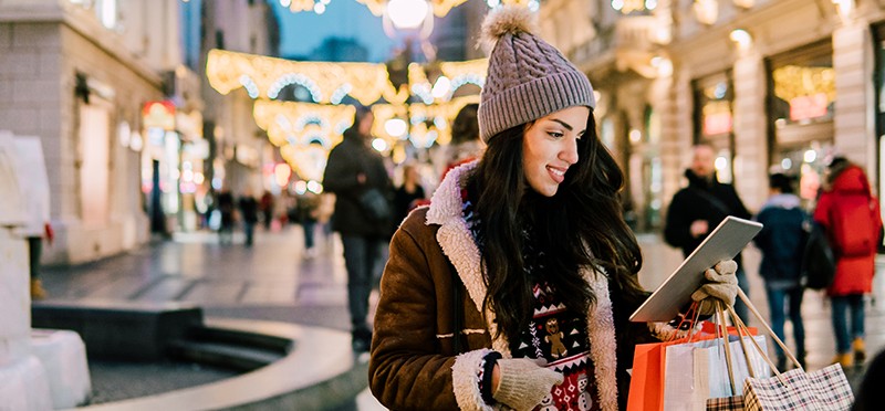 Woman with shopping bags, looking at a tablet in a shopping mall